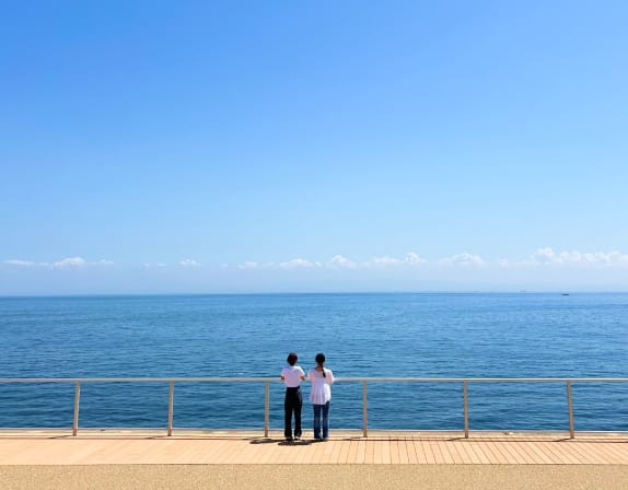 海辺の遊歩道で海を眺める人々の後ろ姿	